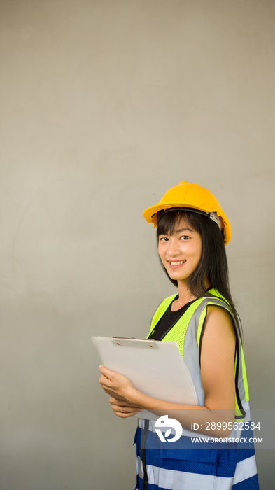 Portrait of a beautiful Asian female engineer cute smile in a reflective vest,hard hat. Female worker with safe working concept at a construction site. Building Construction Project Manager clipboard.