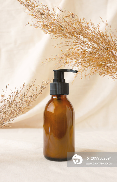 Brown glass bottle with pump for beauty product mockup on linen drapery and dry branch of meadow plant. Concept eco organic cosmetic with natural extracts. Mockup skincare cosmetic product