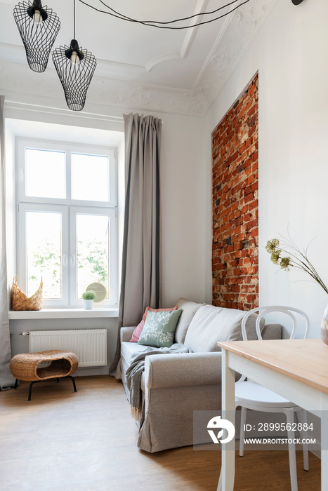 Modern interior of living room with bricky wall, comfortable sofa, table and chair in small apartment with window in hotel. Design architecture. Vertical.