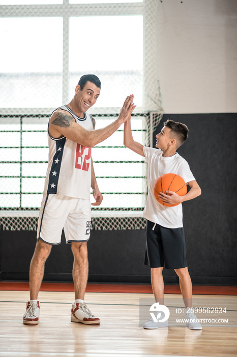 Coach in white sportswear teaching the boy playing basketball