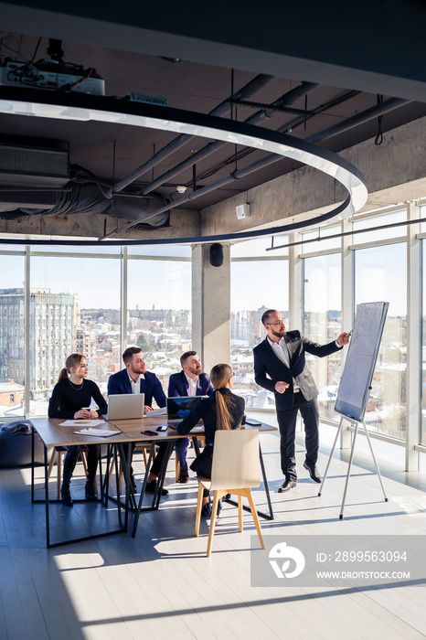 The boss stands near the board with graphs, demonstrates statistics, various personnel attending the training, introduces the new products of the company, reports on the results of work for partners.