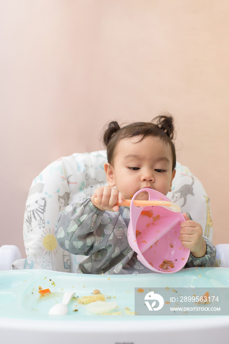 Cute Asian baby girl sitting on dining table practice to use spoon to eat food by her self, Baby-Led Weaning concept