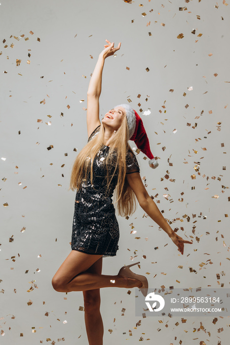 Beautiful blonde Santa girl dancing under glittering confetti. New Year party concept.