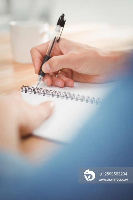 Businessman writing on spiral table at desk