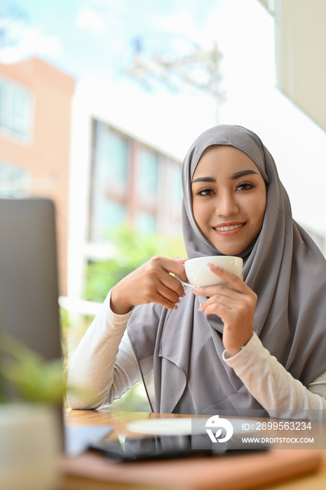 Portrait of an attractive asian muslim lady or businesswoman sipping morning coffee.