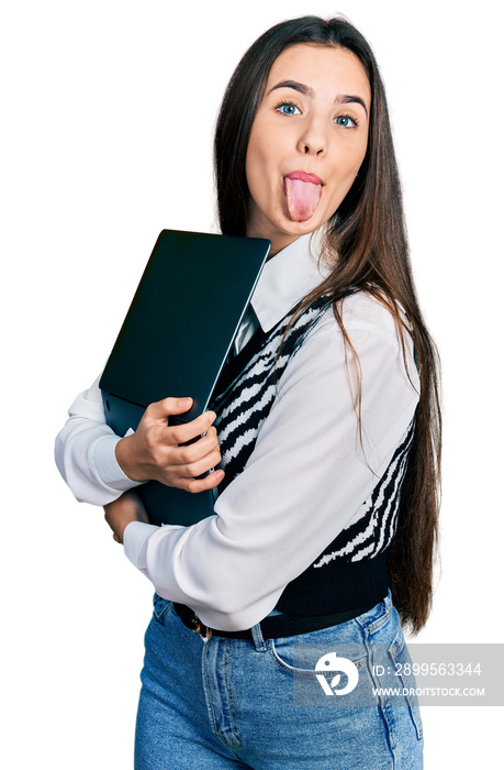 Young brunette teenager hugging laptop with love sticking tongue out happy with funny expression.
