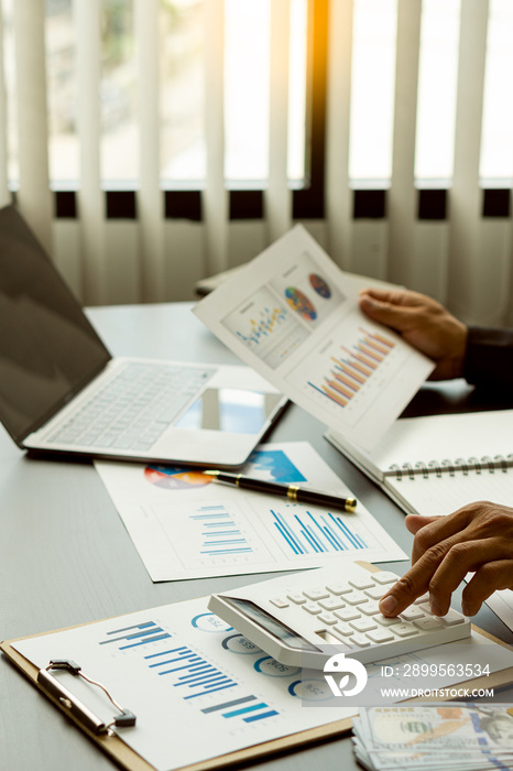 Businessman working with graph papers and laptop calculator to calculate company financial results. On a wooden table in offices and businesses, tax, accounting, statistics and vertical analytical res