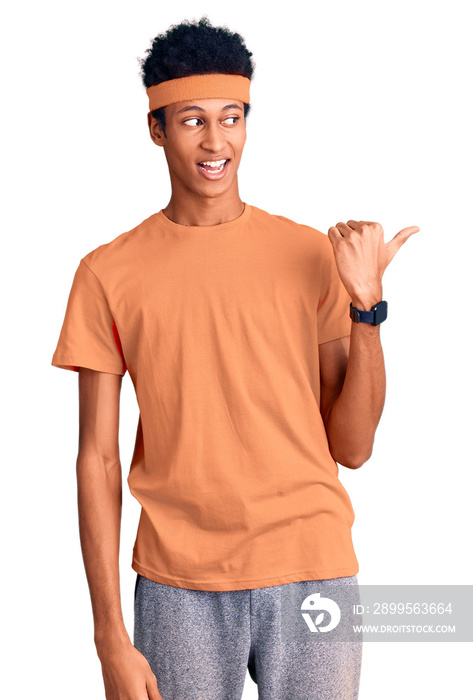 Young african american man wearing sportswear smiling with happy face looking and pointing to the side with thumb up.