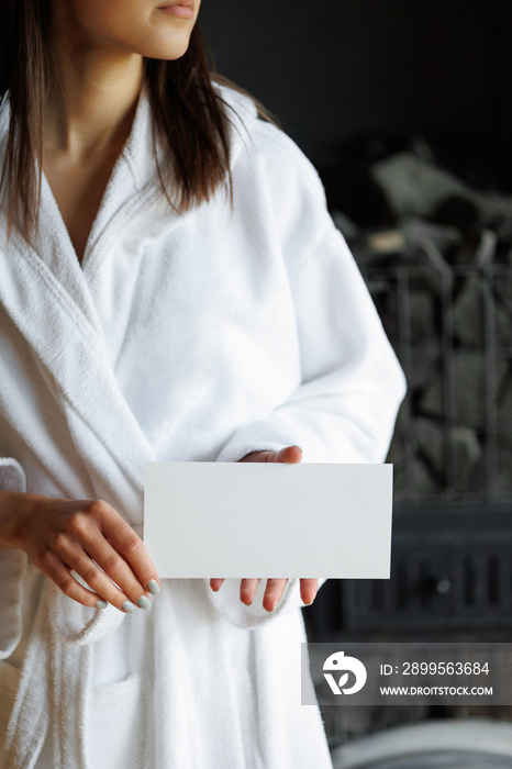 Woman in bathrobe with spa gift voucher in hands