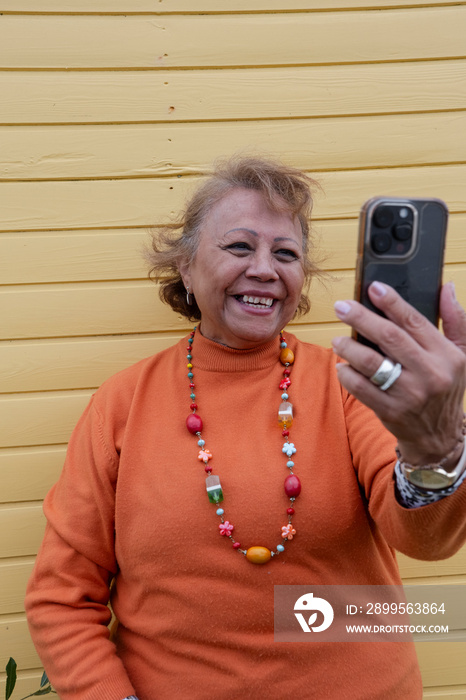 Smiling senior woman using smart phone against yellow wall