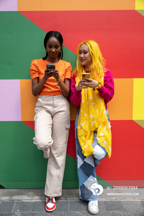 Young female friends using phones outdoors