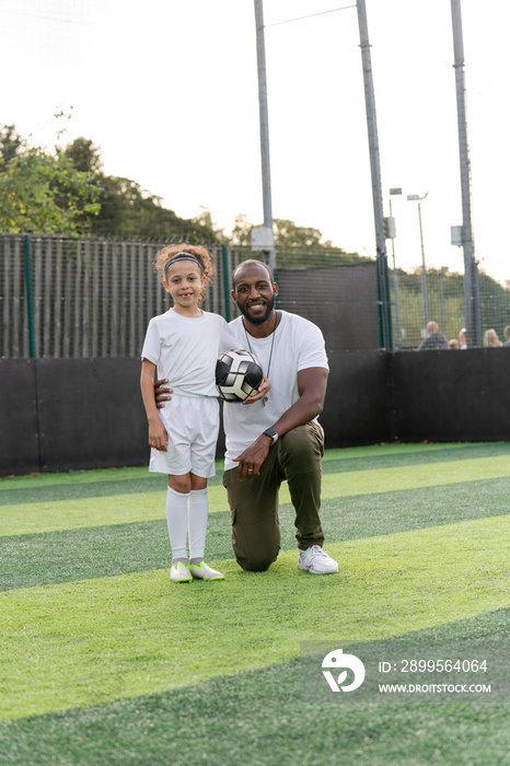 Portrait of man and girl (6-7) with ball on soccer field