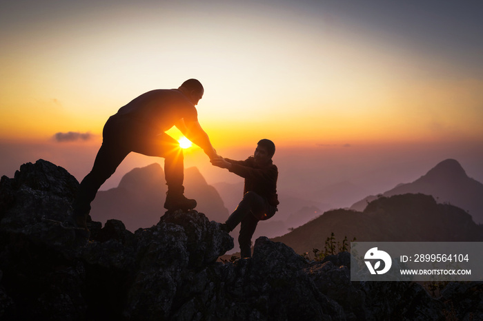 Silhouette Two Male hikers climbing up mountain cliff and one of them giving helping hand. People helping and, team work concept.