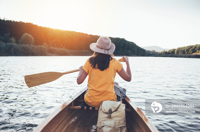 Rear view of woman paddling canoe on the sunset lake