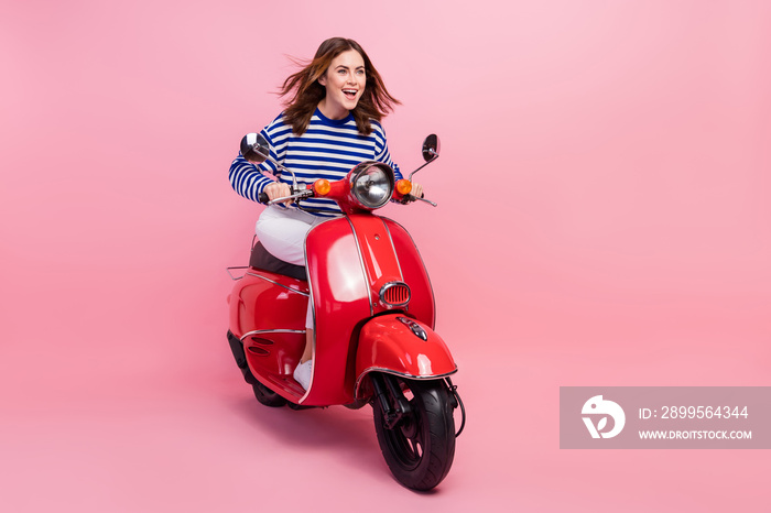 Full size portrait of cheerful pretty girl driving scooter empty space isolated on pink color background