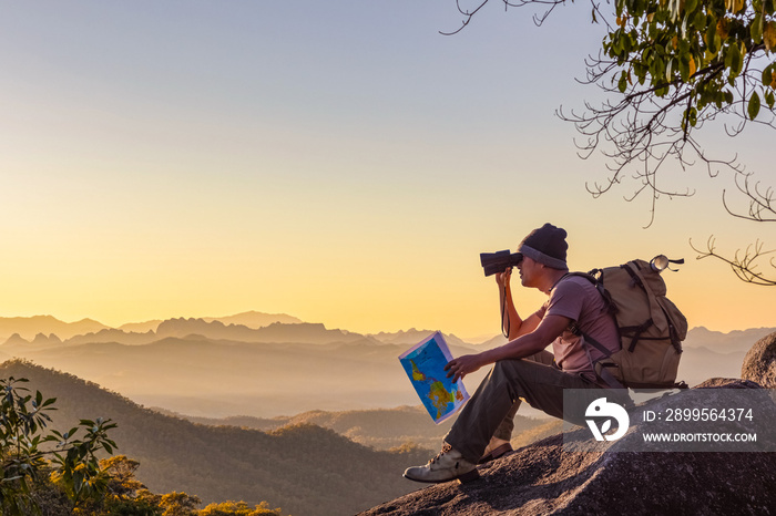 Young man with backpack and holding a binoculars sitting on top of mountain