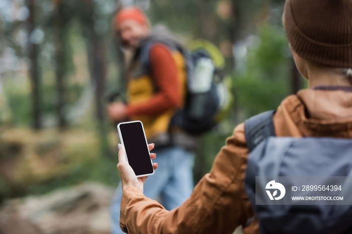 woman holding smartphone while blank screen near blurred man in forest