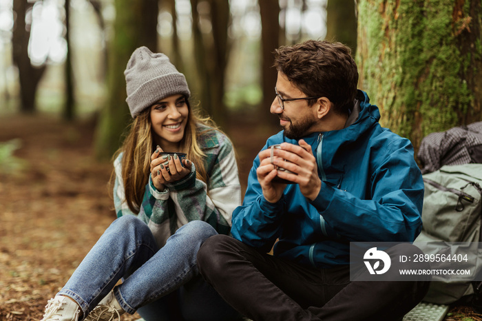 Cheerful millennial caucasian woman and guy in jacket with backpack travel in cold forest, drink hot tea