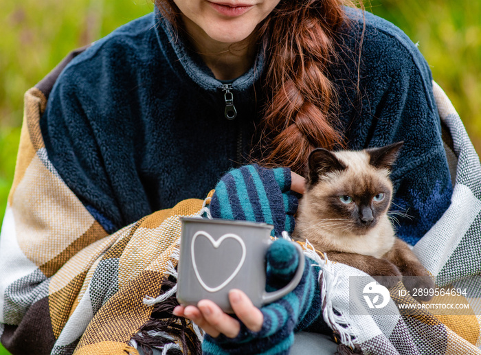 Woman holds a cat and cup of a tea at evening in travel