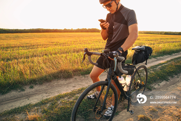 The bike traveler got lost in the middle of field and looking for the route in the smartphone