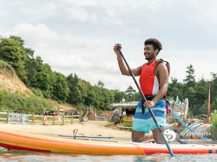 Young man paddleboarding with oar on lake