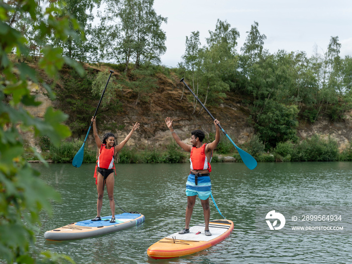 Friends standing with arms raised on paddleboards on lake