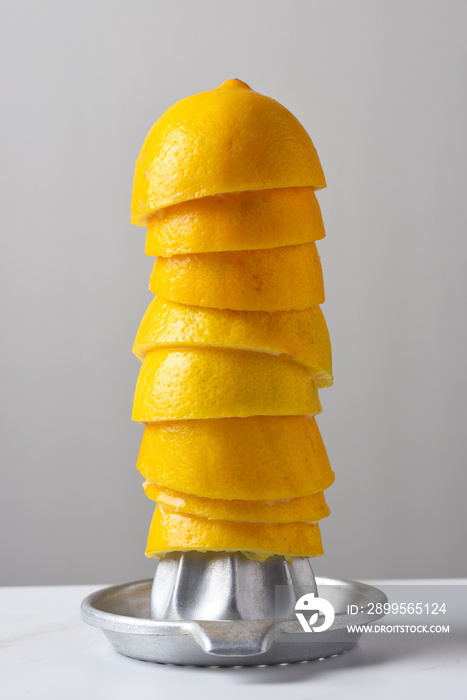 Closeup of a metal hand juicer with a stack of half lemon rinds against a light gray background, leftover form making homemade lemonade.