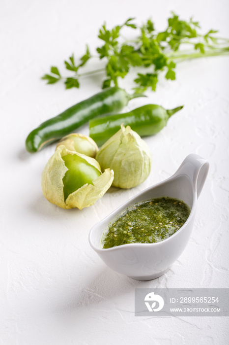 Tomatillo salsa verde. Bowl of spicy green sauce on white table, mexican cuisine.