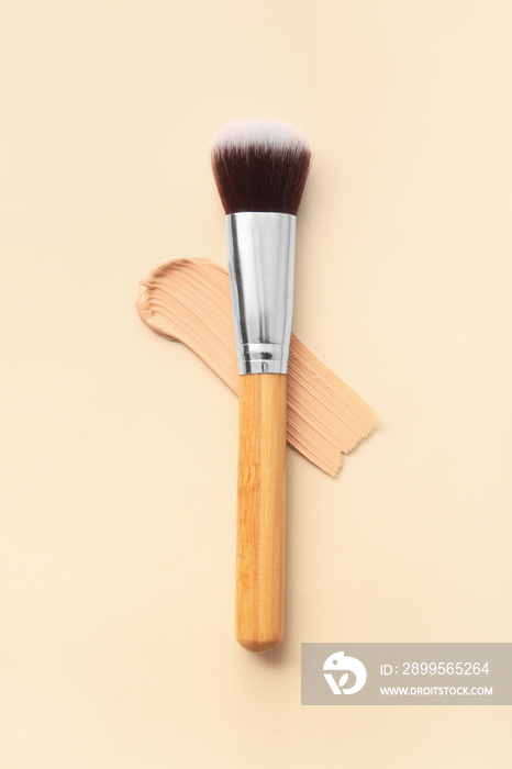 Makeup brush and sample of liquid foundation on color background