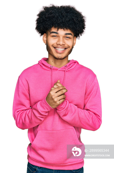 Young african american man with afro hair wearing casual pink sweatshirt with hands together and crossed fingers smiling relaxed and cheerful. success and optimistic