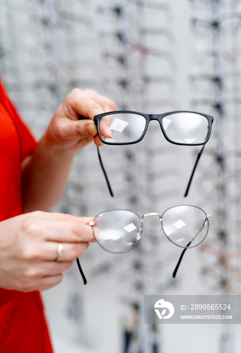 Woman`s hands holding two pairs of glasses in modern frames. Choosing corrective eyewear in optics.