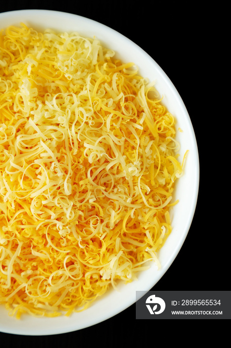 Shredded Mexican Cheese Mix in a White Bowl on a black background, top view. Flat lay, overhead, from above.