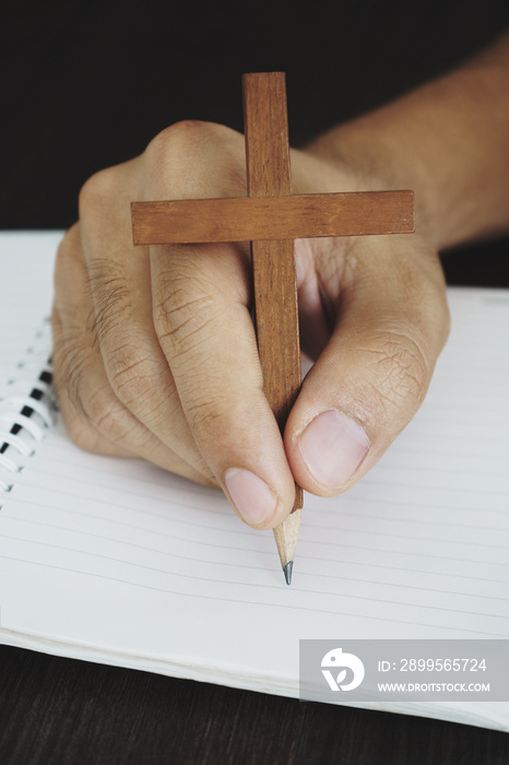 Surreal image of hand writing with wooden cross pencil