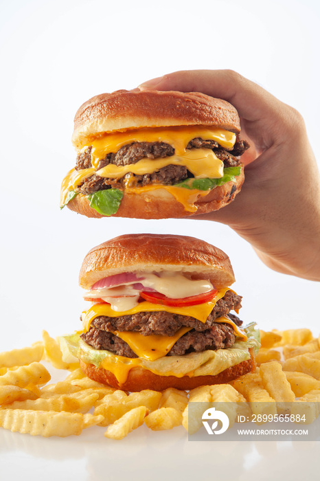 Hand holding a gourmet cheese burger on top of another beef burger with potato chips on the bottom