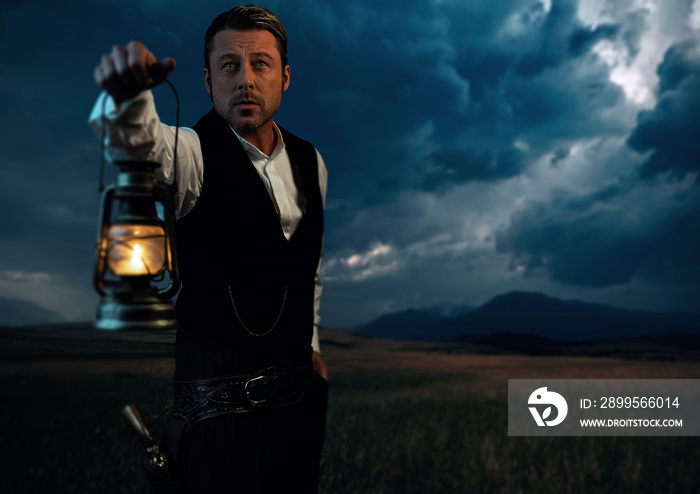 Man in victorian clothing with lantern standing on prairie area.