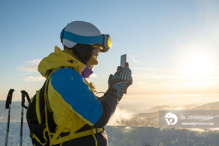 woman skier taking picture of sunset above the mountains