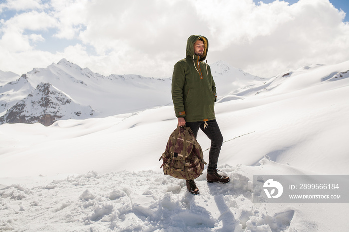 young hipster man hiking in mountains, winter vacation traveling, north, snow, warm clothes, backpack, anorak, jeans, boots