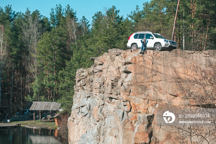 woman relaxing standing at edge of the cliff near lake. suv car.