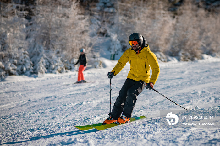 Young person in fashionable clothes is skiing past the camera on a ski slope on a sunny day. Carve or carving on ski piste, perfect weather, strong backlight.