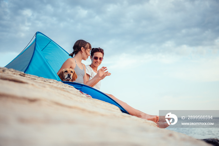 Happy family with dog sitting inside beach tent and having fun