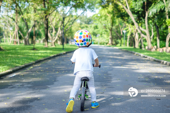 Backside of cute Asian 2 years toddler boy child wearing safety helmet learning to ride first balance bike in sunny summer day, kid cycling at park, Explore & Appreciate Nature with toddlers concept