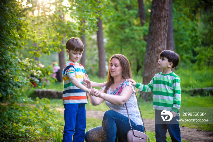 Young woman mother applying insect repellent to her two son before forest hike beautiful summer day or evening. Protecting children from biting insects at summer. Active leisure with kids