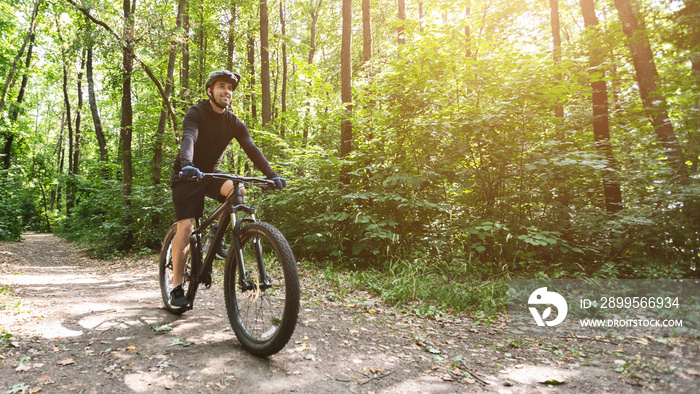 Bicyclist riding by forest road in sun flare