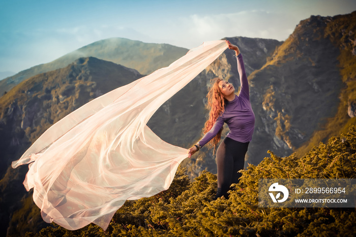 Girl with the light pink fabric playing with wind on mountains