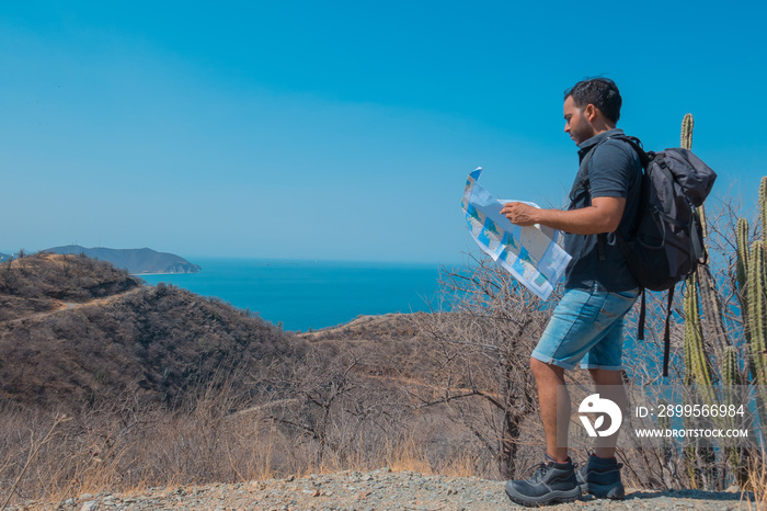 man with boots, map in his hands and backpack on his back, standing on the mountain during travel