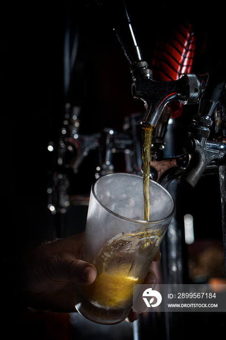 Beer pouring down from tap into cold pint glass at brewery