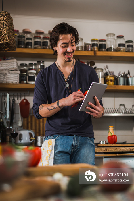 man learns to cook in his kitchen. looking for recipes on digital tablet