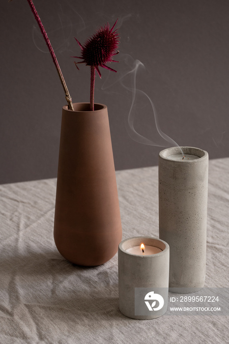 Hygge style composition made up of two candles and clay vase or jug with flowers