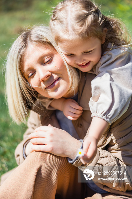 little child holding blurred flower near happy mom outdoors.