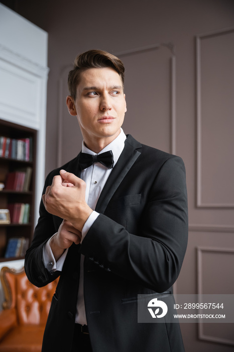 Man in formal wear adjusting sleeve of jacket at home